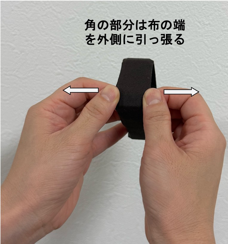 布のシワの伸ばし方その2。片スタの角の部分で、布の端を両手でつまみ、左右の外側へ引っ張っている写真。